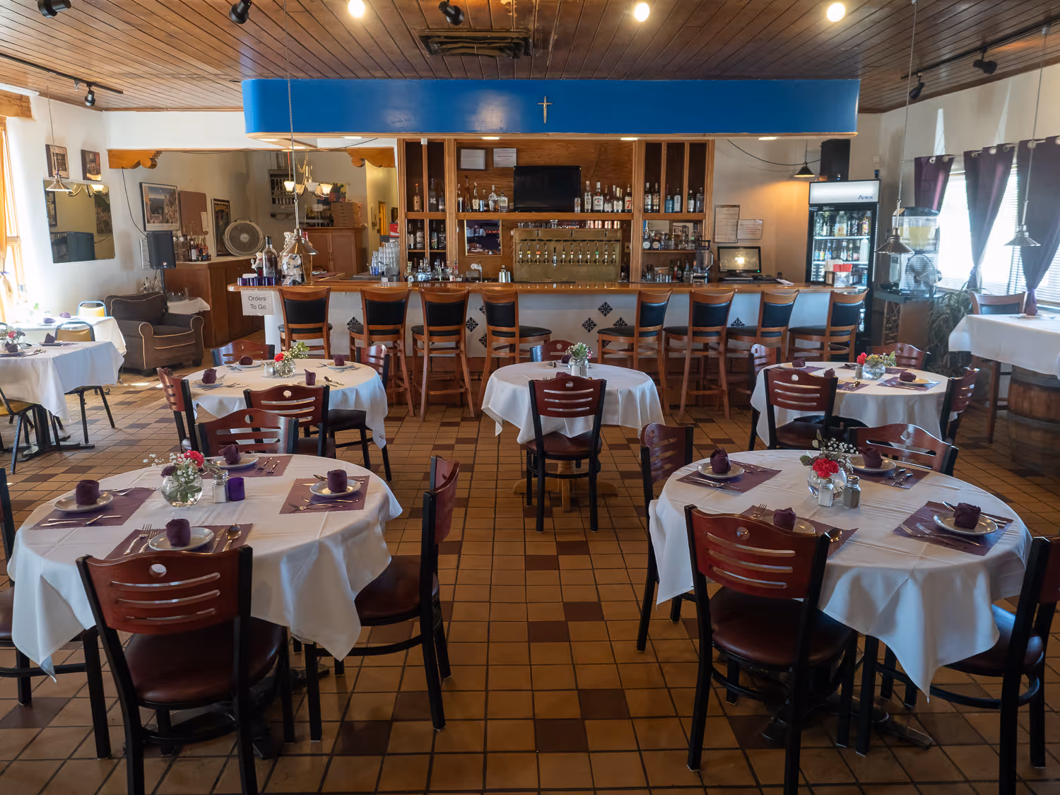 Dining room with round white-clothed tables set with purple napkins, the bar beyond